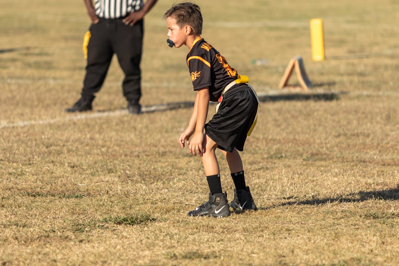 A young boy prepares to play flag football on a grassy field under the sun.