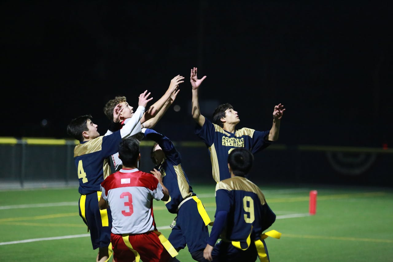 Action-packed nighttime flag football match capturing players in mid-air reaching for the ball.